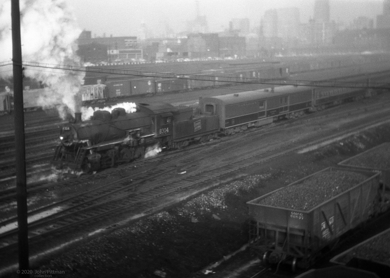 CN 8304 is a class P-5-a 0-8-0 switcher, moving coaches near Spadina Road in downtown Toronto.
Built by ALCo in December 1923, last in a batch of 5 for the GTW, it was transferred to CN in 1942. 
It survived through the end of steam on CN, scrapped in 1961. 
Its first car appears to be lettered "EXPRESS", beyond it are clerestory roof coaches.
At bottom right is a GM&O hopper car, could be a coal load for the nearby Spadina coaling tower.
The switcher's exhaust and vapour suggest that it is reversing toward Toronto Union Station.